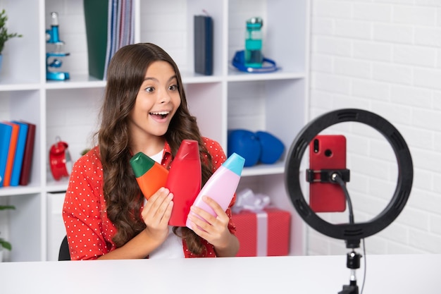 Adolescente segura condicionador de cabelo ou garrafa de xampu gravando vídeo de mídia online Menina adolescente streaming
