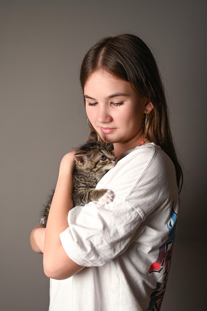 Adolescente segurando um gato bebê em fundo cinza Retrato de jovem com gatinho Crianças e animais de estimação