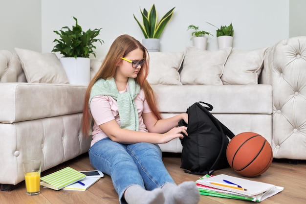 Adolescente sentada en casa en el piso de la sala de estar con libros de mochila