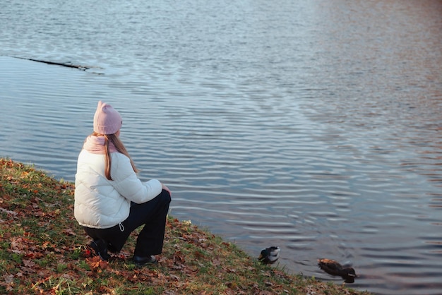 Adolescente sentada por detrás con ropa informal de otoño en un parque de otoño con lago al aire libre