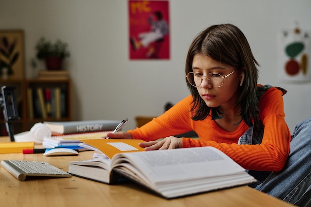 Adolescente sentada en el escritorio con libros y cuadernos y haciendo la tarea en su habitación