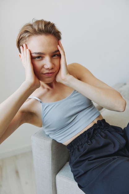 Adolescente sentada no sofá em casa sorrindo em roupas de casa e óculos com um estilo de vida de corte de cabelo curto sem filtros espaço de cópia gratuita