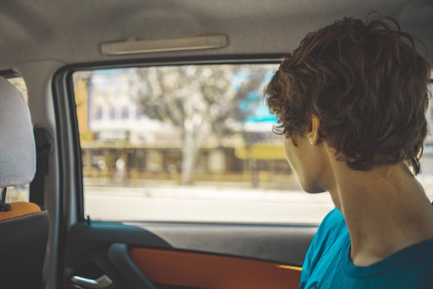 Adolescente sentado en el asiento trasero del coche y mirando por las ventanas