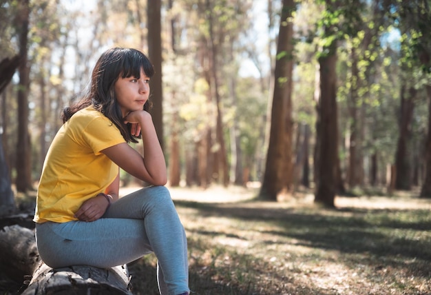 Adolescente sentado em tronco de bosque