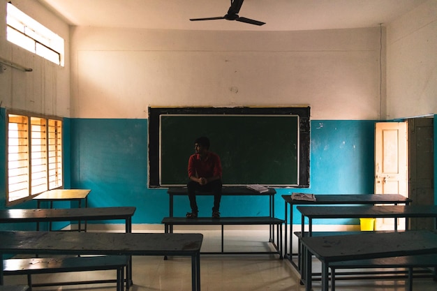 Un adolescente sentado en la mesa frente a la pizarra en la escuela