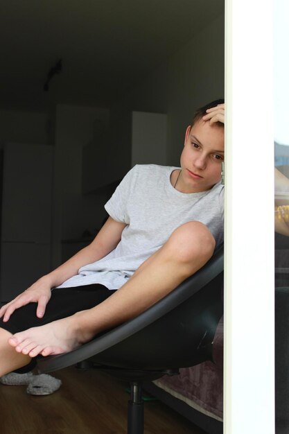 Foto un adolescente está sentado en una puerta abierta y está triste mirando delante de él