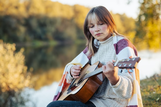 Adolescente séria e concentrada a tocar guitarra na margem do rio.