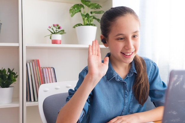 Adolescente ses fones de ouvido sem fio para estudar no computador em casa se comunica na internet acenando olá