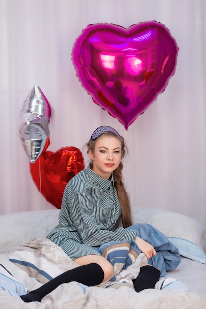 Adolescente se sienta en la cama el día de San Valentín rodeada de globos