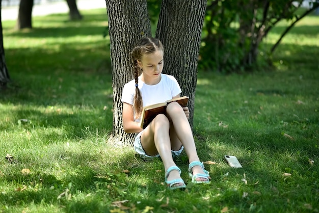 Una adolescente se sienta en la hierba verde y lee un libro Educación Infancia