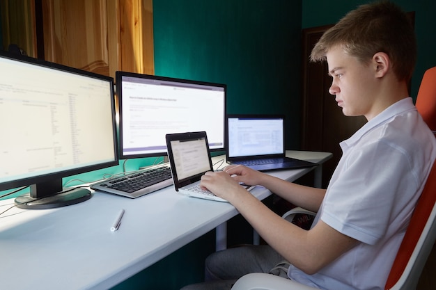 Un adolescente se sienta y mira detrás de muchos monitores.