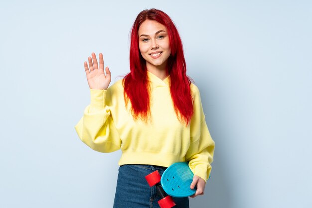 Adolescente skater mujer aislada en la pared blanca saludando con la mano con expresión feliz