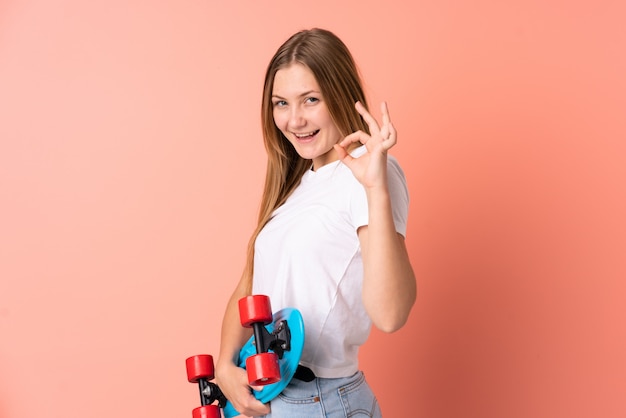 Adolescente skater ucraniana chica aislada en rosa con un patín y haciendo signo OK