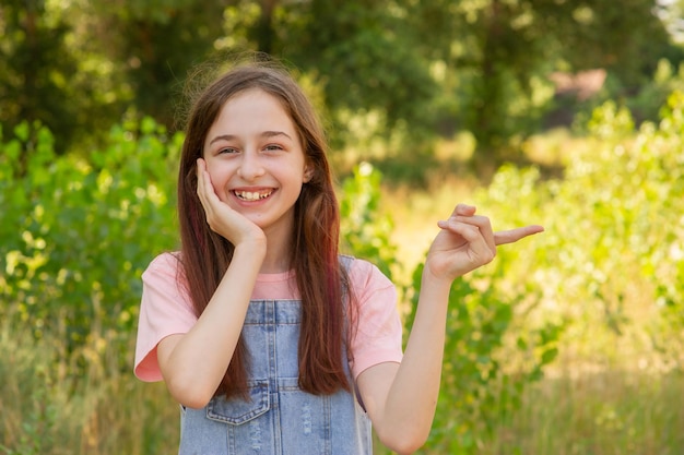 Una adolescente sonríe y señala con el dedo índice hacia un lado. Chica en el fondo de la naturaleza.