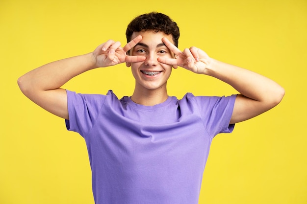 Adolescente sonriente y atractivo con ropa informal gesticulando mostrando el signo de la victoria con los dedos