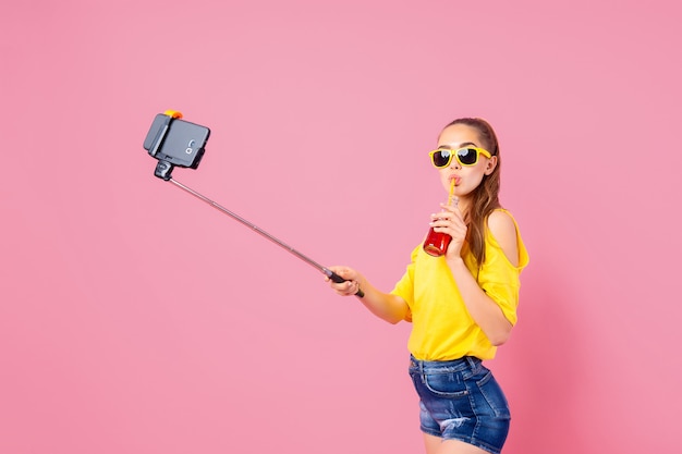 Adolescente sonriente con bebidas haciendo selfie con palo