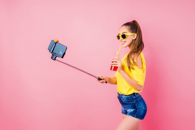 Adolescente sonriente con bebidas haciendo selfie con palo