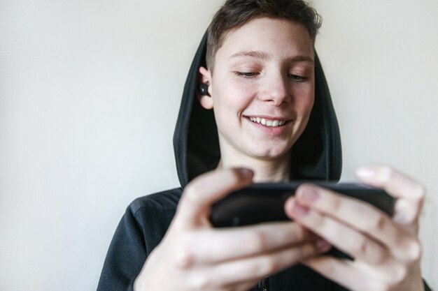 Un adolescente sonriente en una capucha negra y auriculares habla por teléfono