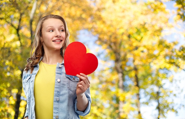 Foto una adolescente sonriente con un corazón rojo en el parque de otoño