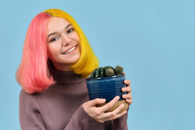 Una adolescente sonriente con un disparo en la cabeza con el pelo teñido de color sosteniendo una olla con cactus