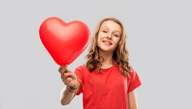 una adolescente sonriente con un globo en forma de corazón rojo