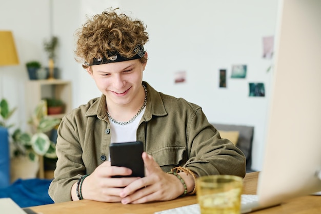 Un adolescente sonriente mirando la pantalla de su teléfono inteligente mientras ve un video
