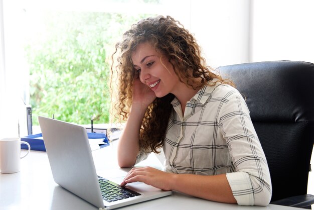 Adolescente sonriente sentado en el escritorio con la computadora portátil