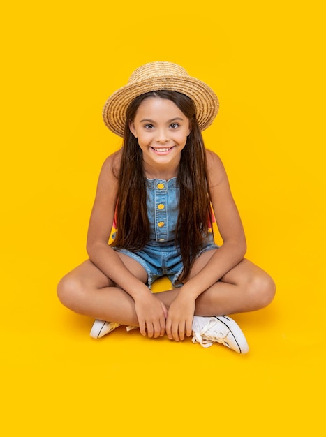 Una adolescente sonriente con sombrero de paja sentada en un fondo amarillo