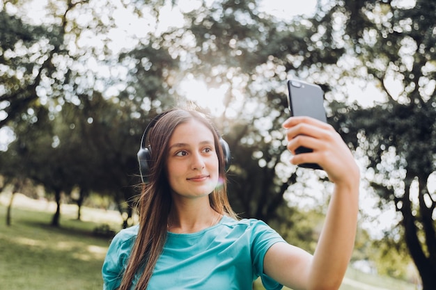 Adolescente sonriente, tomándose un selfie con su móvil en el parque