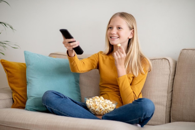 Una adolescente sonriente viendo la televisión y comiendo palomitas de maíz en un sofá