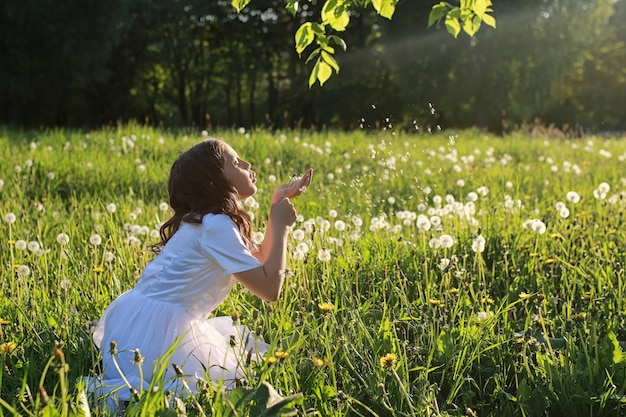 Un adolescente soplando semillas de una flor de diente de león en un parque de primavera