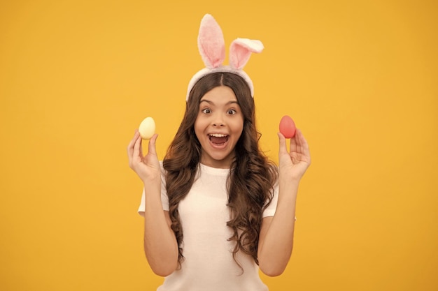 Una adolescente sorprendida con orejas de conejo sostiene huevos en la pascua de fondo amarillo