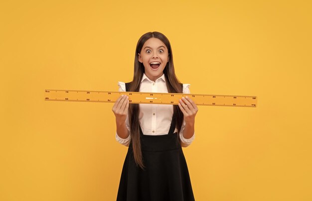 Una adolescente sorprendida con uniforme escolar sostiene una regla matemática para medir la escuela