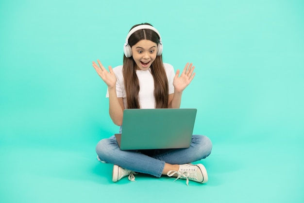 Una adolescente sorprendida usa una computadora portátil inalámbrica para una videollamada o escucha un seminario web en auriculares comprados en línea