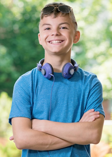 Adolescente sorridente de 1214 anos com as mãos cruzadas Estudante adolescente com fones de ouvido e óculos de sol posando ao ar livre