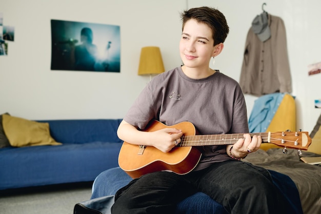 Adolescente sorridente em roupa casual tocando guitarra acústica em casa