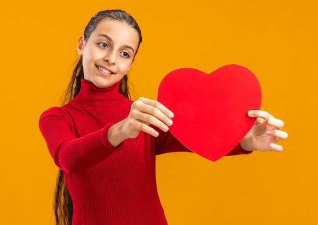 Adolescente sorridente se espreguiçando e olhando para o formato de um coração isolado na parede laranja