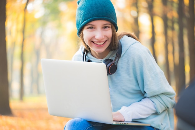 Adolescente sorridente sentada no banco com um laptop