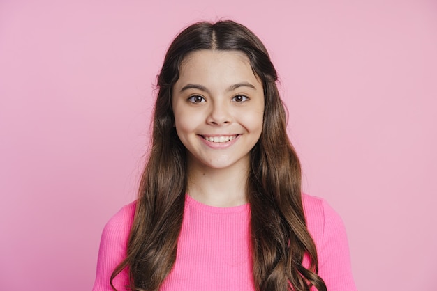 Adolescente sorridente, sorrindo sinceramente em um fundo rosa. A garota olha para a câmera