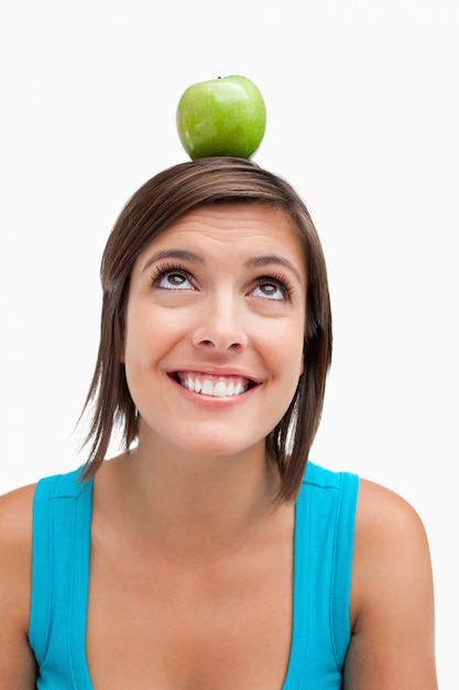 Foto adolescente sorridente tentando olhar para uma maçã verde colocada em sua cabeça