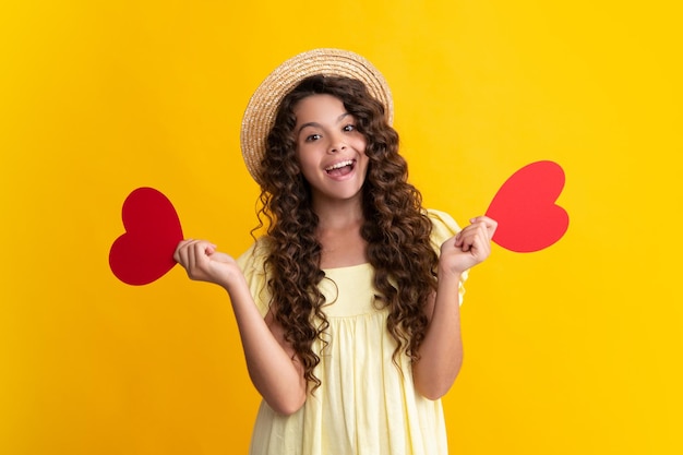 Adolescente sostenga forma corazón signo de forma de corazón Niño sosteniendo un corazón rojo amor vacaciones San Valentín símbolo aislado sobre fondo amarillo Feliz adolescente emociones positivas y sonrientes de niña adolescente