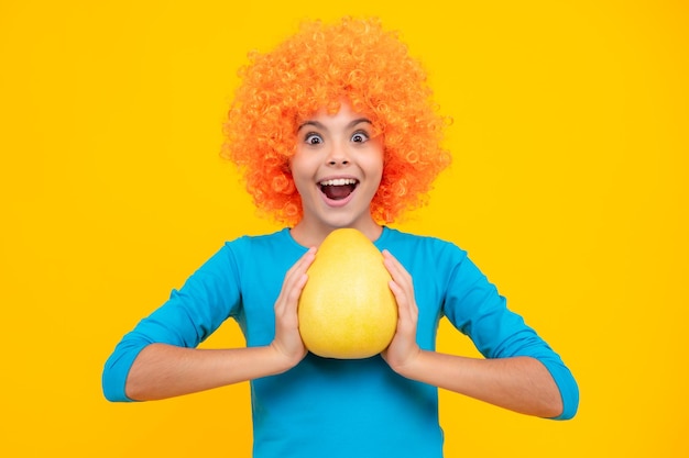 Foto adolescente sostiene pomelo de cítricos o pomelo aislado sobre fondo amarillo frutas de verano adolescente emocionado contento asombrado y lleno de alegría emociones