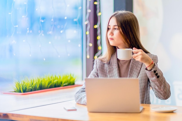 Una adolescente sostiene una taza de café mirando por la ventana.