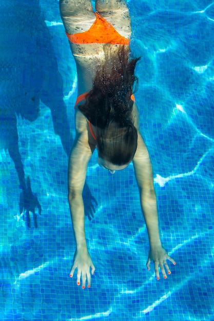 Adolescente submerso debaixo d'água na piscina. Fundo azul. Conceito de verão