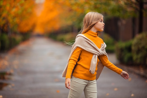 una adolescente con un suéter amarillo camina por una calle fuera de la ciudad con el telón de fondo de árboles amarillos divertido caminar en otoño