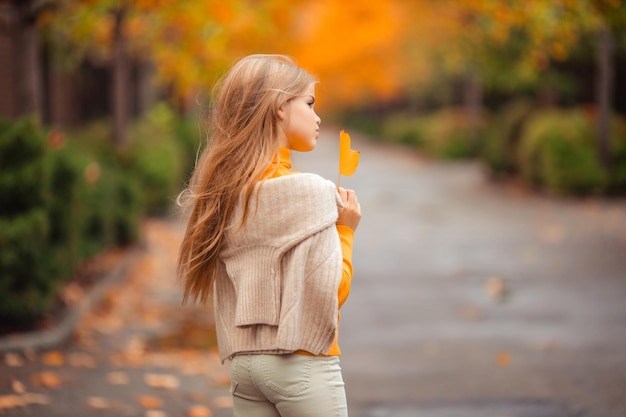Foto una adolescente con un suéter amarillo camina por una calle fuera de la ciudad con el telón de fondo de árboles amarillos divertido caminar en otoño