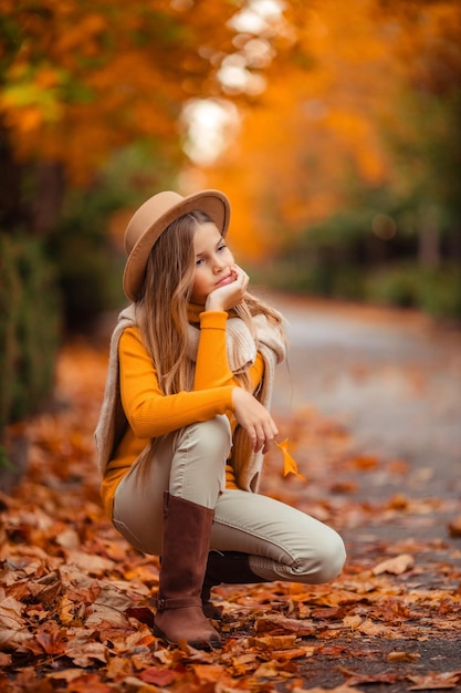 Foto una adolescente con un suéter amarillo camina por una calle fuera de la ciudad con el telón de fondo de árboles amarillos divertido caminar en otoño