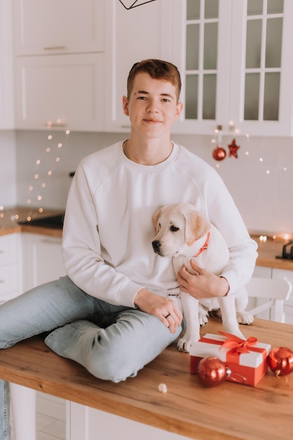 Un adolescente con un suéter blanco abraza a su amado perro en una cocina bellamente decorada para Navidad. cuidar una mascota. vacaciones familiares y fines de semana. espacio para texto. foto de alta calidad