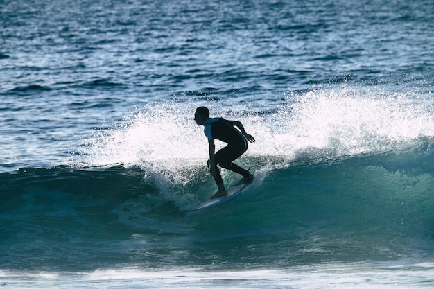 Foto adolescente surfeando en la ola en tenerife playa de las americas - trajes de neopreno blanco y negro y ola hermosa y pequeña