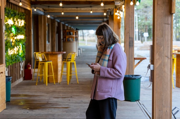 Una adolescente con un teléfono inteligente en la terraza de un café al aire libre en el parque